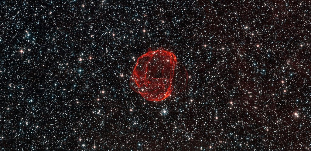 These delicate wisps of gas make up an object known as SNR B0519-69.0, or SNR 0519 for short. The thin, blood-red shells are actually the remnants from when an unstable progenitor star exploded violently as a supernova around 600 years ago. There are several types of supernova, but for SNR 0519 the star that exploded is known to have been a white dwarf star — a Sun-like star in the final stages of its life. SNR 0519 is located over 150 000 light-years from Earth in the southern constellation of Dorado (The Dolphinfish), a constellation that also contains most of our neighbouring galaxy the Large Magellanic Cloud (LMC). Because of this, this region of the sky is full of intriguing and beautiful deep sky objects. The LMC orbits the Milky Way galaxy as a satellite and is the fourth largest in our group of galaxies, the Local Group. SNR 0519 is not alone in the LMC; the NASA/ESA Hubble Space Telescope also came across a similar bauble a few years ago in SNR B0509-67.5, a supernova of the same type as SNR 0519 with a strikingly similar appearance. A version of this image was submitted to the Hubble’s Hidden Treasures Image Processing Competition by Claude Cornen, and won sixth prize.
