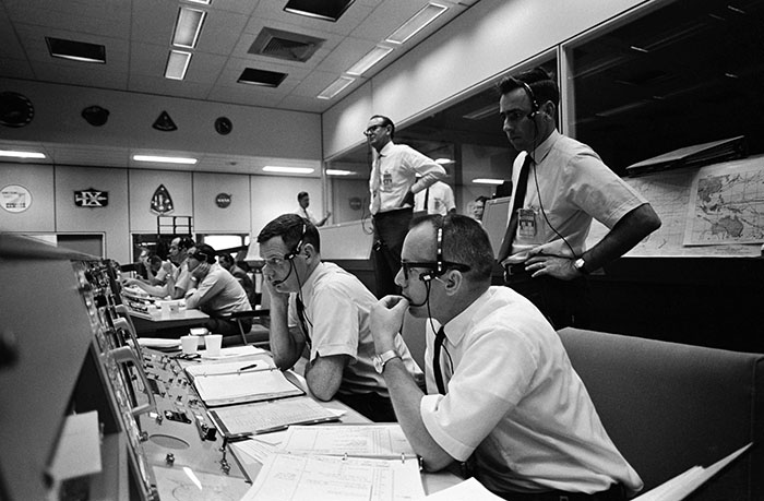 Date Created: 1969-05-19 View of activity at the flight director's console in the Mission Operations Control Room in the Mission Control Center, Building 30, on the first day of the Apollo 10 lunar orbit mission. Seated are Gerald D. Griffin (foreground) and Glynn S. Lunney, Shift 1 (Black Team) flight directors. Milton L. Windler, standing behind them, is the flight director of Shift 2 (Maroon Team). In the center background, standing, is Dr. Christopher C. Kraft Jr., MSC Director of Flight Operations.