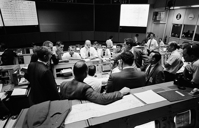 Date Created: 1970-04-16 Overall view showing some of the feverish activity in the Mission Operations Control Room (MOCR) of the Mission Control Center (MCC) during the final 24 hours of the problem-plagued Apollo 13 mission. Here, flight controllers and several NASA/MSC officials confer at the flight director's console. When this picture was made, the Apollo 13 lunar landing had already been canceled, and the Apollo 13 crewmembers were in trans-Earth trajectory attempting to bring their crippled spacecraft back home.
