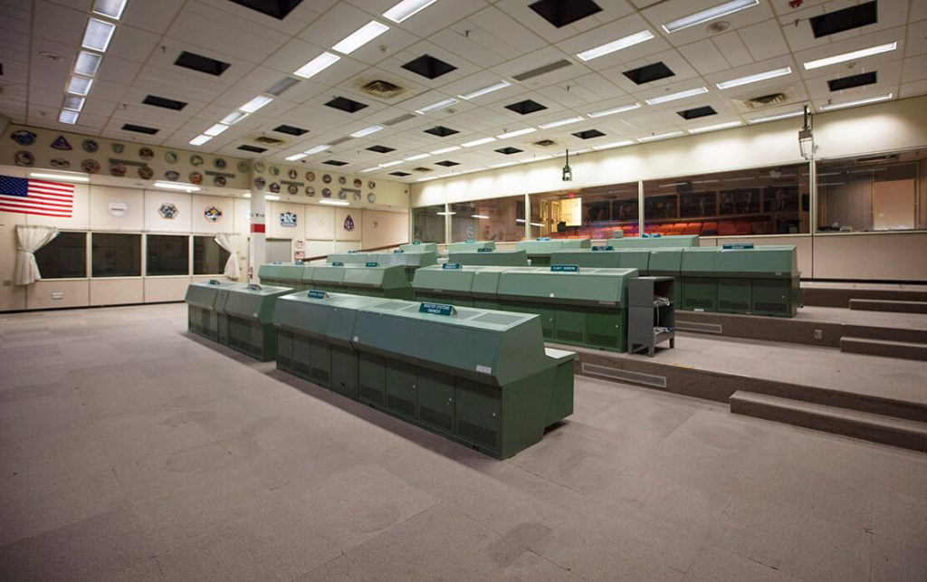 A front view of the iconic green consoles in Historic Mission Control. After decades of use, the carpet in the room has become stained and is deteriorating.